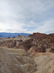 Fototapeta premium A sweeping view of undulating hills in earthy tones, leading to rugged peaks under a soft cloudy sky.