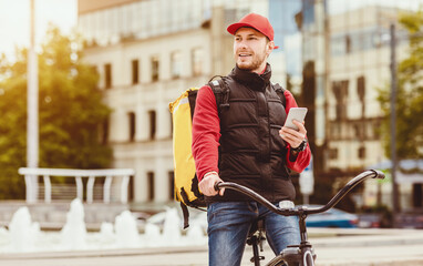Delivery App Concept. Courier Man Using Mobile Phone Delivering Food Riding Bicycle Outdoors In...