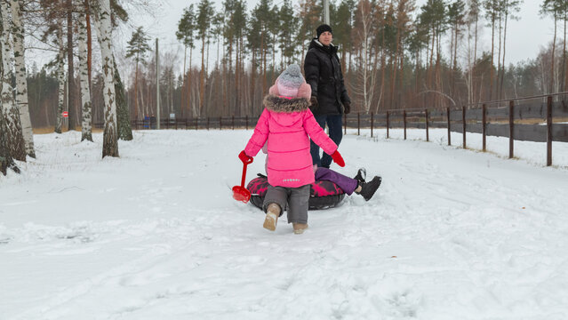 Father and daughters ride downhill on a Snow tubing in the park on the winter holidays