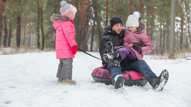 Child girls with dad riding snow tube on sunny winter morning. Funny games on winter vacation.
