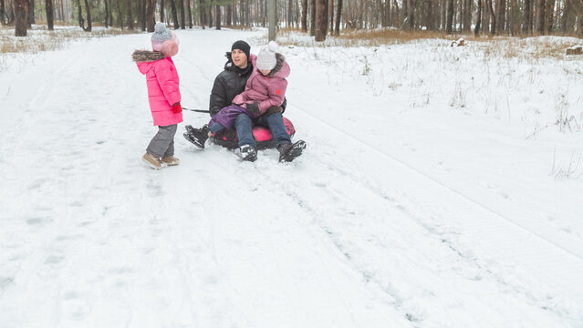 Child girls with dad riding snow tube on sunny winter morning. Funny games on winter vacation.