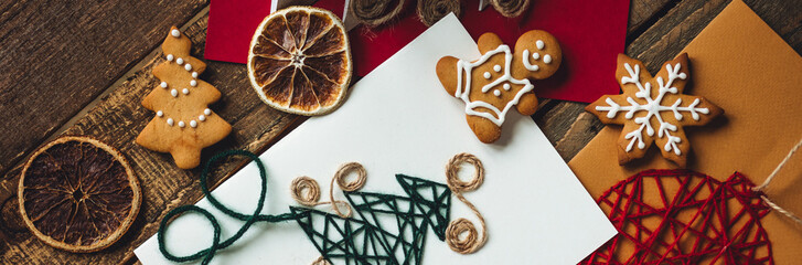 Banner flat lay. Preparation for a holiday season. Handmade children greeting postcards. Embroidered, origami fir tree, gingerbread cookies. Recyclable materials, eco friendly gift. Wooden background