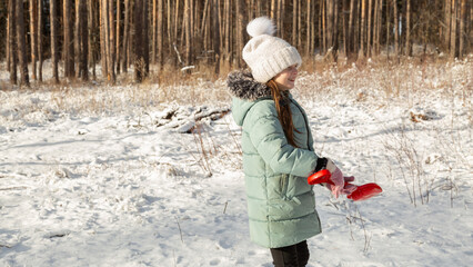Cheerful positive child girl wearing a outerwear smiling walking through a snowy countryside forest