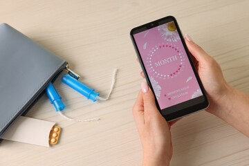 Menstruation. Woman using period calendar application on smartphone at wooden table, above view