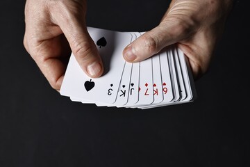 Illusionist shuffling playing cards on black background, closeup
