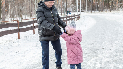 Little girls with her grandfather walking in park on snowy winter day