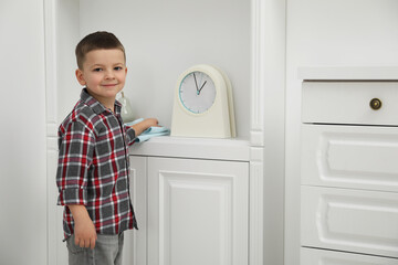 Little helper. Cute boy wiping dust from chest of drawers at home