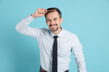 Handsome man stylish his hair with comb on light blue background