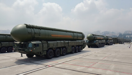 Long rows of military vehicles carry large ballistic missiles in a secure compound under a clear sky. The scene highlights military readiness and transport logistics during daylight