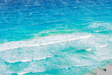 Turquoise waves of Caribbean Sea with white foam rolling toward shore under bright sunlight, view from high balcony. Cancun. Mexico.