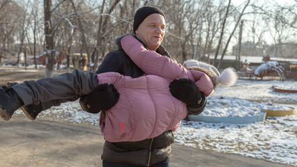 Grandfather playing with her granddaughter on the playground in the park in winter