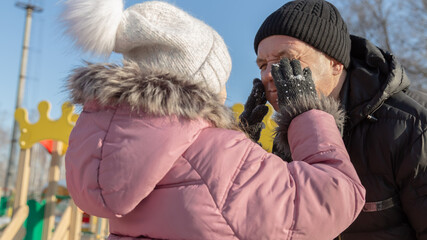 Grandfather playing with her granddaughter on the playground in the park in winter