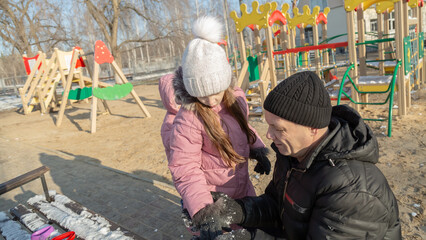 Grandfather playing with her granddaughters on the playground in the park in winter