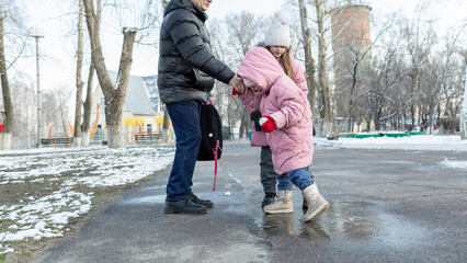 Grandfather walks with his granddaughters after school in the park in sunny winter day