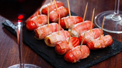 Roasted miniature sausage links wrapped in smoky bacon. Tasty appetizer for wine