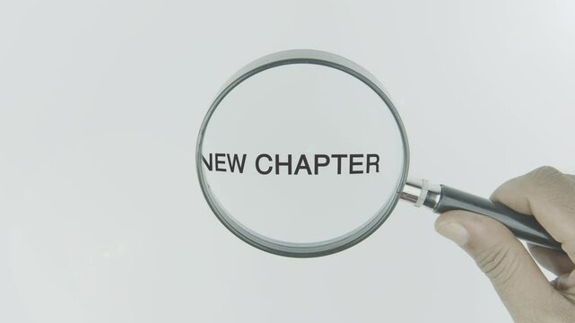New chapter text or word highlighted by a magnifying glass in a hand on a white background, symbolizing a fresh start, transition, and new phase in life or a story