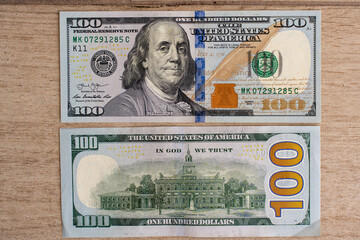 Modern 100 US dollar bill front and back sides on wooden surface. Concept of financial security, wealth, investment, and economic stability. Detailed close-up of currency design and security features.