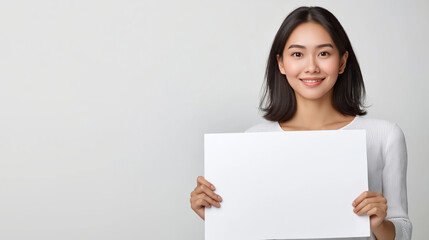 Fototapeta premium Businesswoman grinning, gripping blank whiteboard against neutral studio backdrop, offering clean marketing canvas for creative branding message
