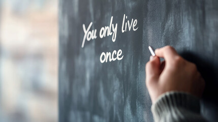 Close up of a teacher's hand writing the motivational message you only live once on a blackboard with chalk