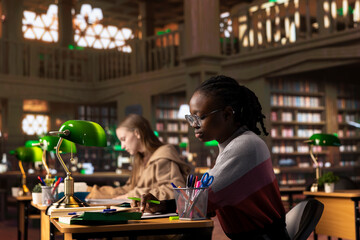 African american girl highlighting important handwritten class notes to integrate in her diploma paper with citations from reliable academic sources within the library database. Research collection.