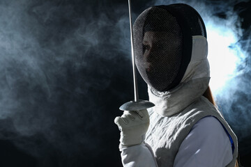 Fencer with epee in smoke on black background, space for text