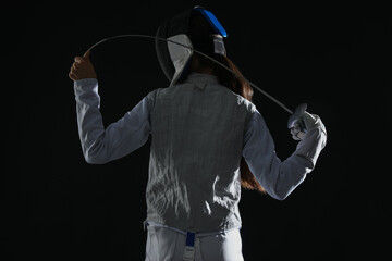 Fencer with epee on black background, back view