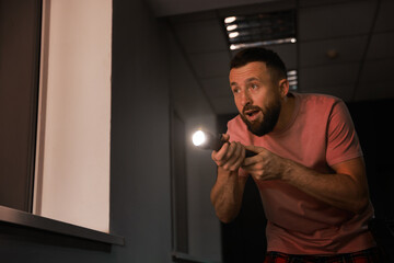 Fear of darkness. Scared man with flashlight indoors at night