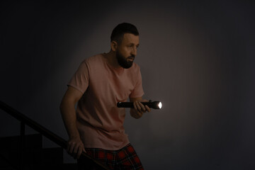 Fear of darkness. Scared man with flashlight indoors at night, space for text