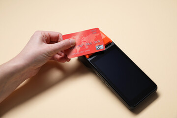 Woman with credit card using payment terminal on beige background, closeup