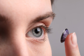 Woman putting in color contact lens on grey background, closeup