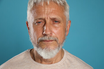 Sad senior man crying on light blue background, closeup