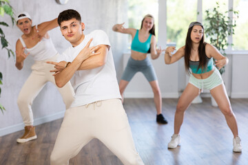Portrait of cheerful teenage guy practicing krumping movements during group dance lesson in studio