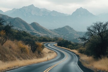 Fototapeta premium Winding mountain road through a serene landscape. A paved road curves through a valley nestled amongst rolling hills and distant mountains. 