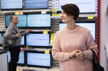 Portrait of a thoughtful European woman standing in the department with televisions in an...
