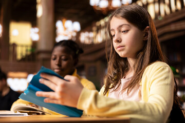 Diverse scholars focused on reading books at the school library, focusing on literature and...
