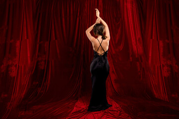 Elegant woman in a black evening dress standing before a vibrant red textile curtain, exuding beauty
