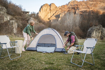 mature couple husband and wife hikers set up a tent together in nature