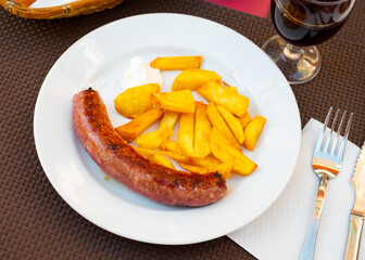 Fried potatoes and treditional spanish pork sausage butifarra on white plate