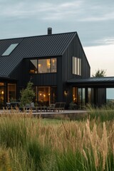 Obraz premium Modern black house set against a serene landscape with tall grasses at dusk, showcasing large windows and contemporary design elements in nature