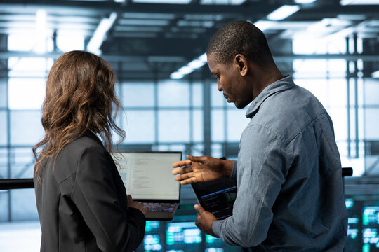 Programmers in data center facility workplace use laptop to calibrate supercomputers energy usage. Server room IT staff members code on notebook, doing maintenance on equipment rigs