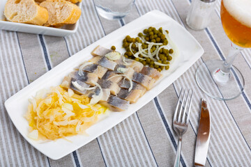 Light salted herring with pickled cabbage and green peas dished up in a plate on the laid table