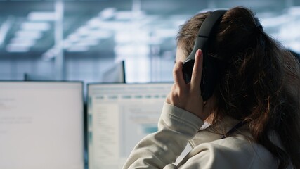 Engineer typing on computer in server hub, checking recovery plan, monitoring data center energy consumption, listening music. Technician wearing headphones inspecting rackmounts, camera A close up