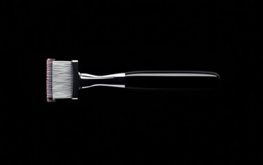 Black handled brush with white and red bristles against a black background. Close-up studio shot