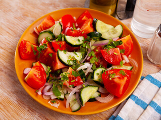 Colorful salad with fresh ripe tomatoes, green cucumbers, sliced red onion and herbs. Vegetarian appetizer