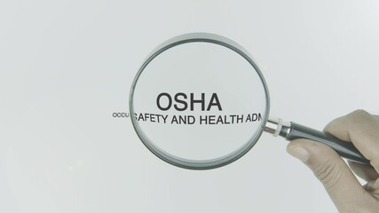 OSHA or Occupational Safety and Health text or word highlighted by a magnifying glass in a hand on a white background, symbolizing focus on workplace safety, regulations, and health standards