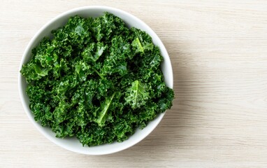 Fresh green kale leaves in a white bowl on a light wooden background. Overhead view.  Healthy eating concept