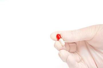 Gloved hand holding a red capsule on isolated white background. Medicine, health, treatment and pharmaceutical concept. Close up of hand fingers with a single pill. Copy space