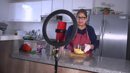 Senior woman preparing food, recording video tutorial in kitchen - Powered by Adobe