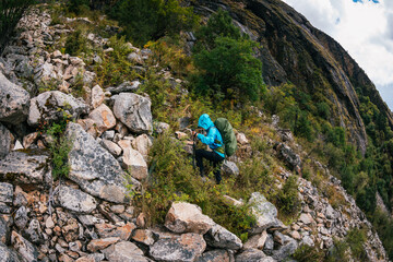Backpacking woman climbing up on steep cliff edge at high altitude mountains top