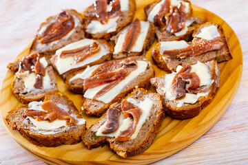 Tasty canapes with butter and salted anchovies served on wooden board